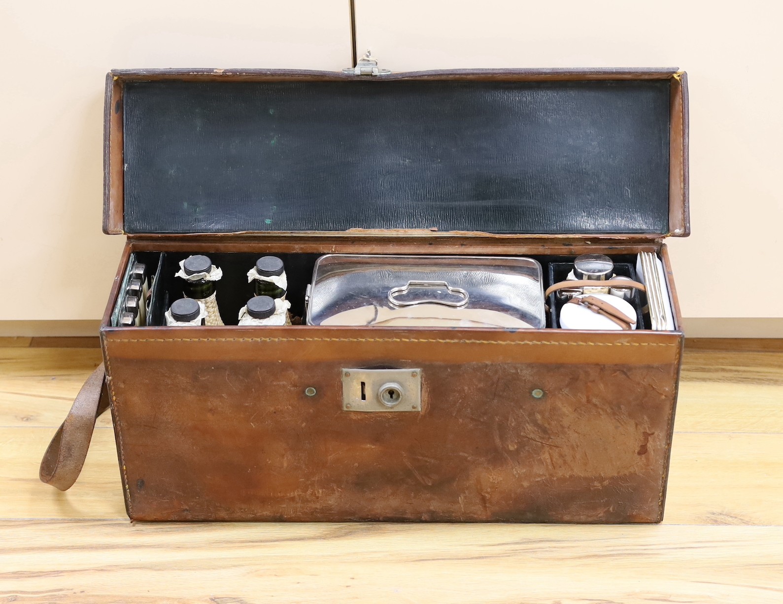 Automobilia related - an early leather cased car picnic hamper, with enamelled plates, basket work covered glass bottles and tumblers and plated cutlery
